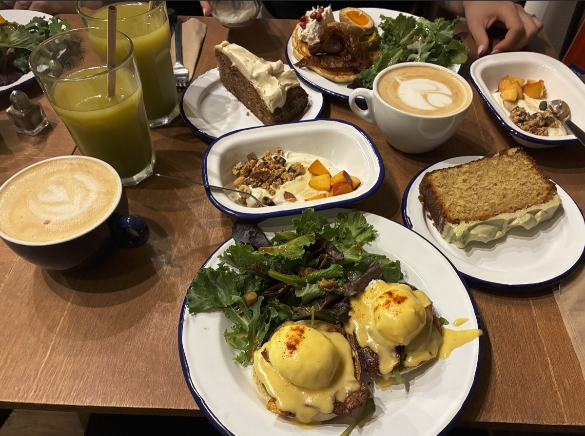 Brunch table with eggs Benedict, coffee, juice, cake, and yogurt bowls
